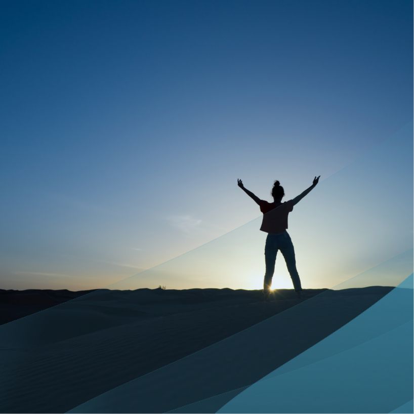 Woman celebrating at the top of a cliff on a hike at sunset