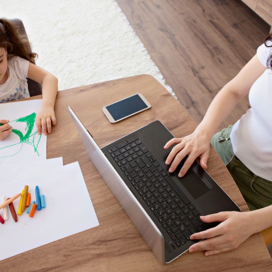 mom on her laptop while her daughter colors