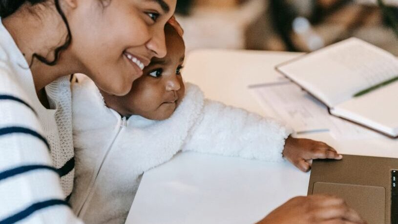 Woman on computer taking an online course while holding child