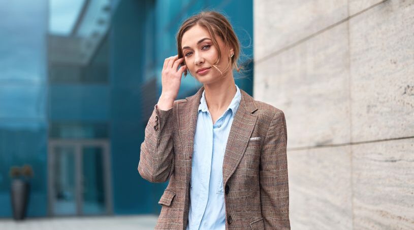 Business woman brushing hair out of her face in front of a modern building