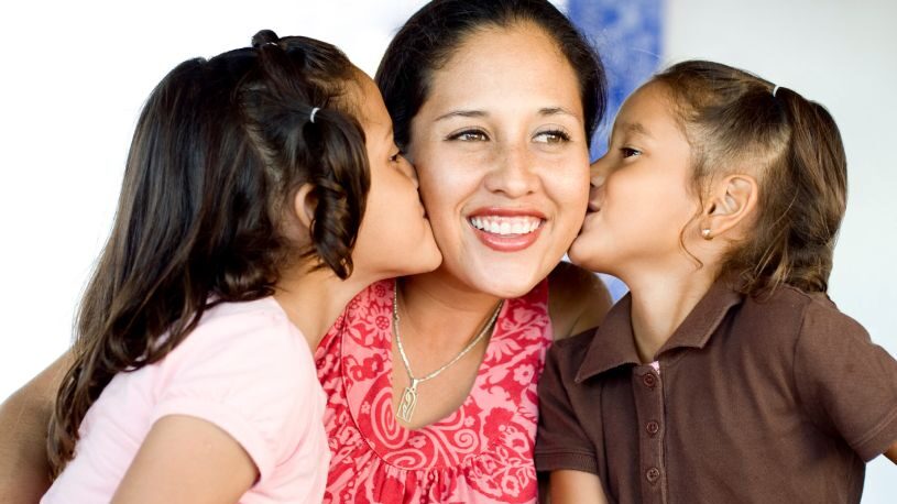 mother being kissed by two daughters