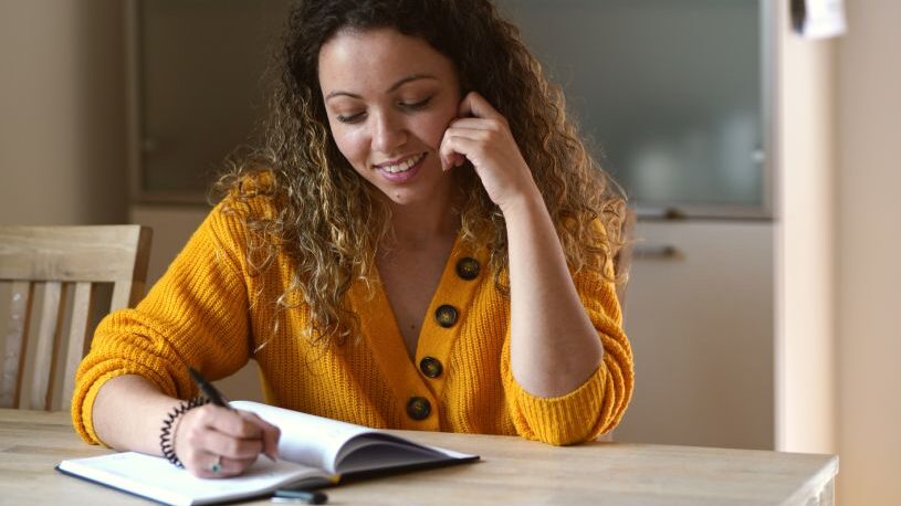 Happy woman taking notes at the kitchen table