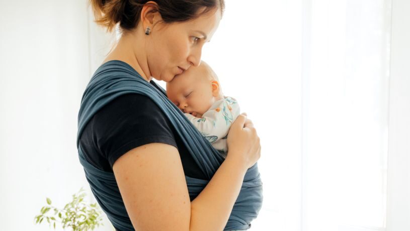 Mother holding infant in a soft carrier wrap